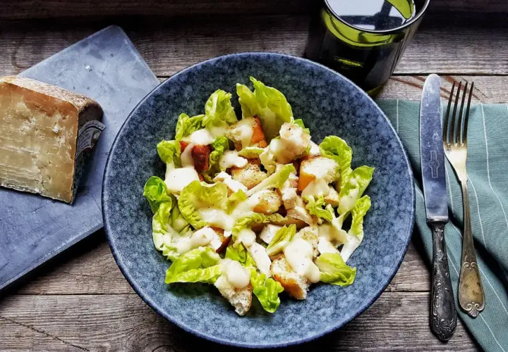Insalata Caesar con crostini e una generosa spolverata di crema di pecorino. Accanto, un pezzo di formaggio stagionato.