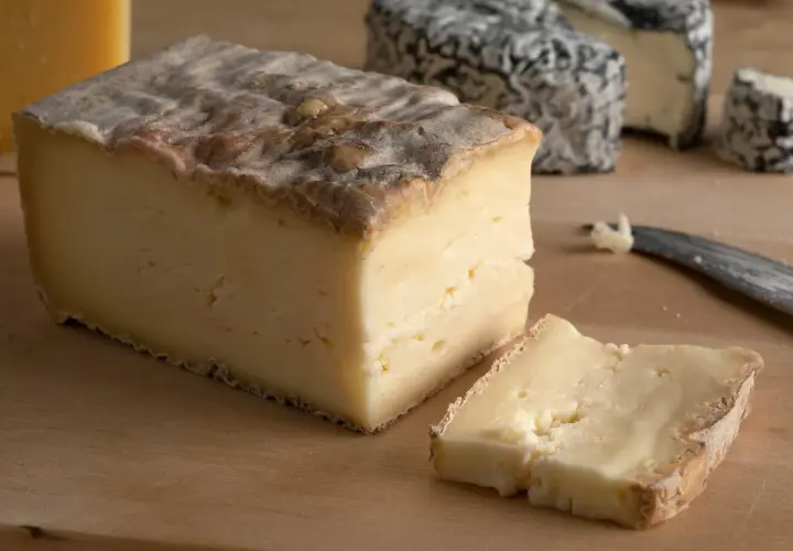 Un pezzo di taleggio dal sapore intenso, con una fetta tagliata e altri formaggi sullo sfondo.