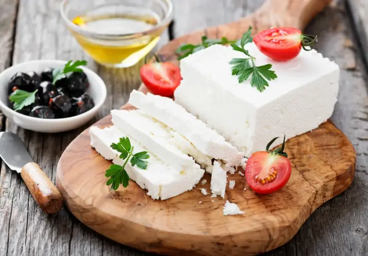 Una porzione feta fresca, tagliata a fette, con pomodorini e olive nere su un tagliere di legno.