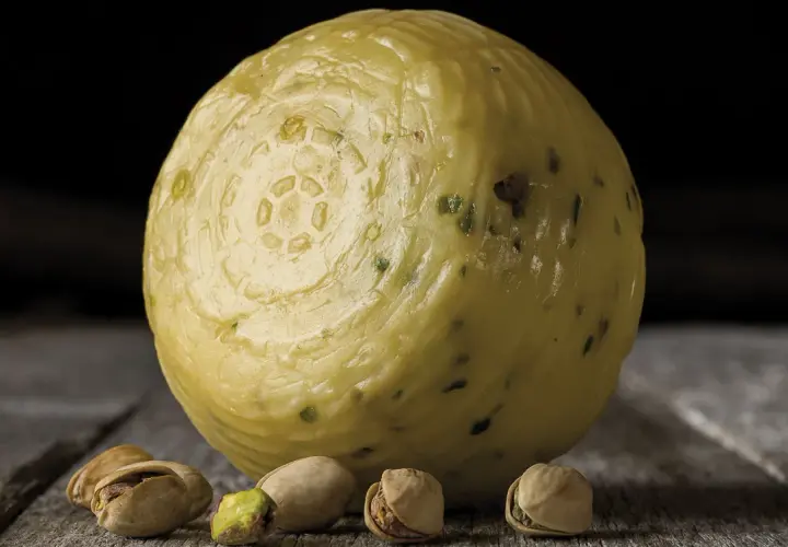 Formaggio pecorino al pistacchio, con alcuni pistacchi sparsi sul tavolo di legno.