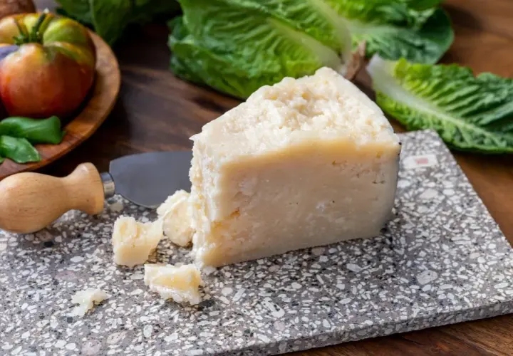 Un pezzo di pecorino siciliano stagionato, pronto per essere gustato con pomodori e lattuga fresca.