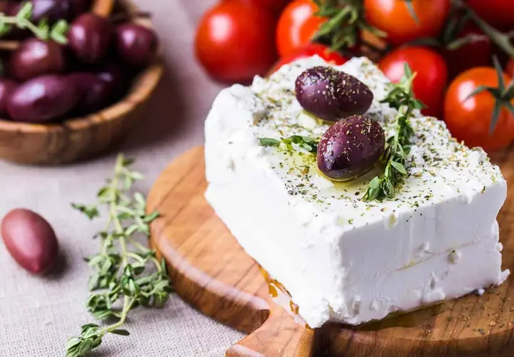 Blocco di feta condito con olive e erbe aromatiche, perfetto per scoprire quante calorie ha la feta in una gustosa insalata greca.