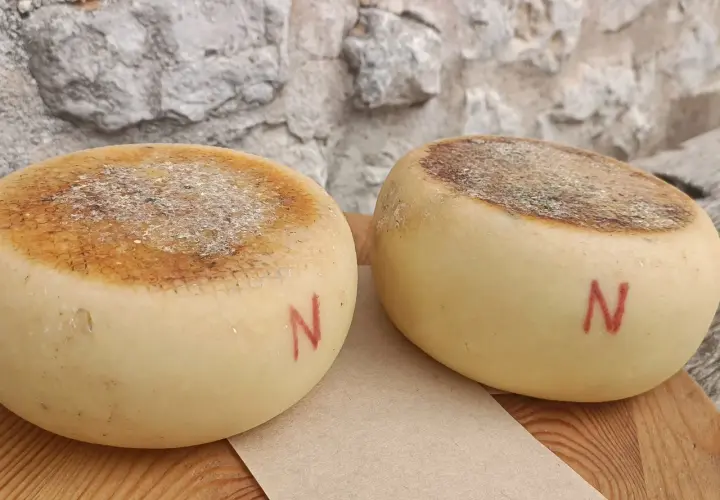 Due forme di pecorino semistagionato, con la crosta marcata e la lettera "N" rossa dipinta sul fianco, riposano su un tagliere di legno.