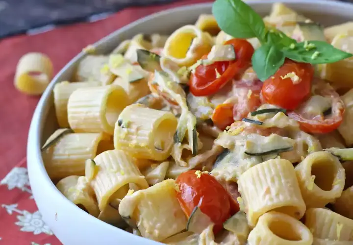 Piatto cremoso di pasta con zucchine, pomodorini e Philadelphia, guarnito con basilico fresco.