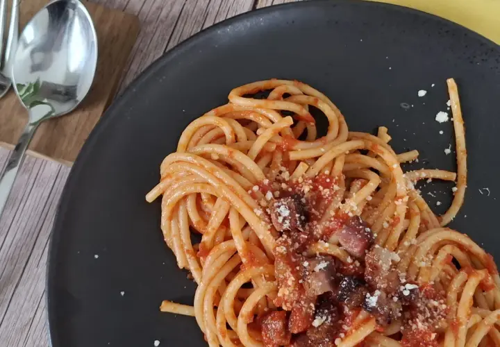 Un piatto di pasta all'amatriciana fumante, con guanciale croccante e pecorino grattugiato, pronto per essere gustato.