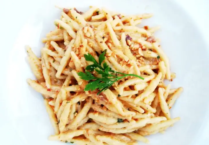 Un piatto di trofie cacio e pepe, condite con una cremosa salsa al formaggio e pepe, guarnite con prezzemolo fresco.