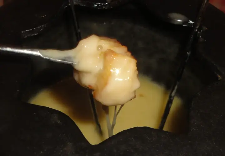 Un pezzo di pane intinto nella fonduta savoyarde ricetta, filante e dorato, pronto per essere gustato.