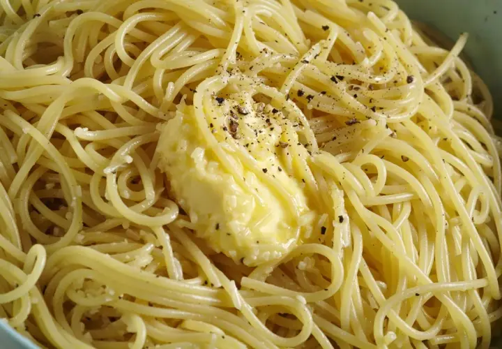 Un piatto di spaghetti fumanti, conditi con burro fuso e pepe nero macinato, pronti per essere gustati come un classico cacio e pepe.