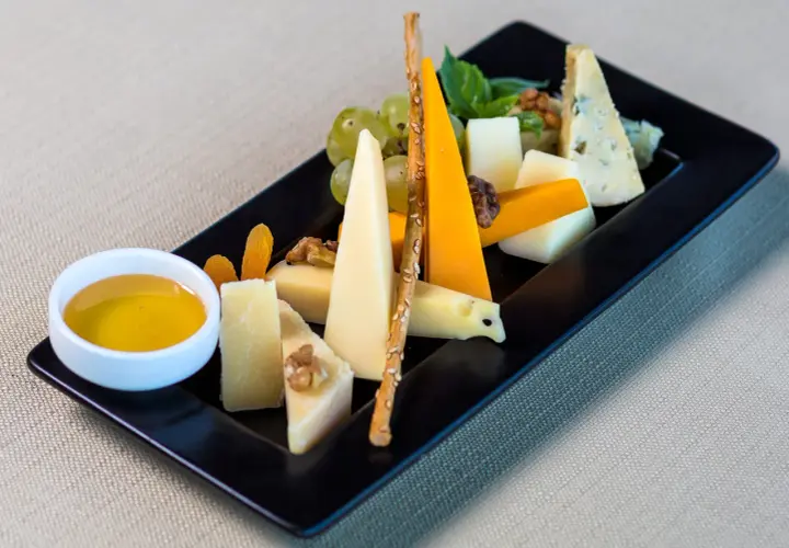 Piatto nero con vari formaggi, uva, noci, albicocche secche, grissini e una ciotolina di miele. Perfetti abbinamenti formaggi e frutta per un aperitivo.