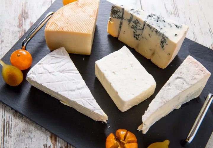 Assortimento di formaggi, tra cui un cremoso formaggio morbido, un erborinato e altri tipi, guarniti con frutta.