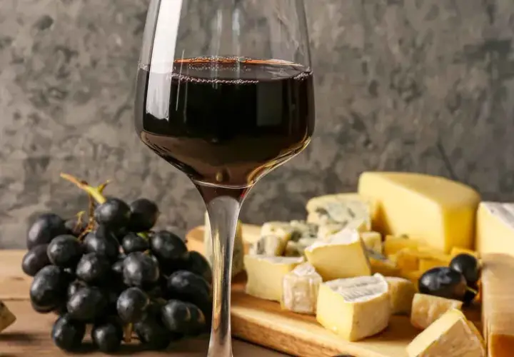 Un bicchiere di vino rosso accompagna un invitante tagliere di formaggi misti, con uva nera e un coltello da formaggio.
