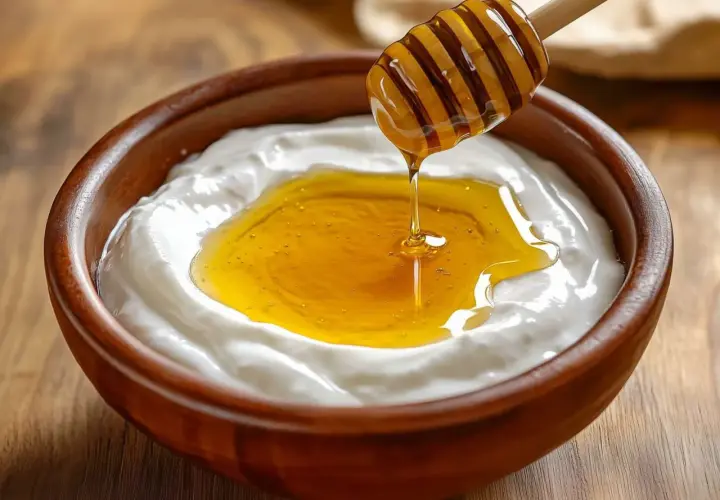 Un cucchiaio di miele cola su uno yogurt cremoso in una ciotola di legno. Attenzione, yogurt e miele fa ingrassare se consumati in eccesso!