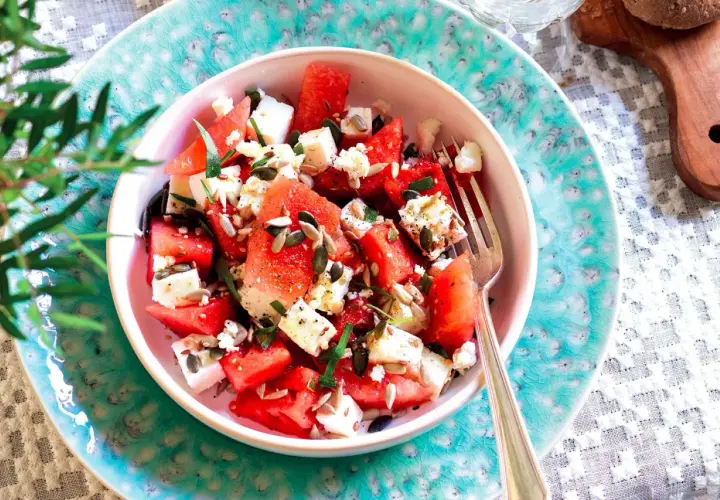 Insalata anguria e feta, fresca e colorata, con semi di girasole e zucca, guarnita con erbe aromatiche. Perfetta per l'estate.