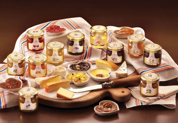 Una selezione di conserve, tra cui composta di fichi per formaggi, salse dolci e confetture, disposte su un tagliere con formaggi.