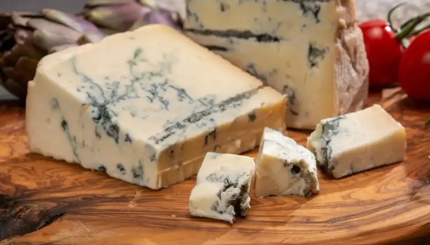 Pezzi di gorgonzola su tagliere di legno, con carciofi e pomodorini. Un assaggio dell'autentica gorgonzola origine.