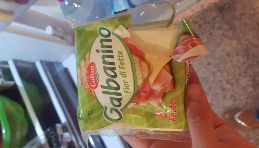 Una mano tiene una confezione di Galbanino Fior di Fette, con prosciutto e formaggio visibili. Perfetto per uno spuntino in gravidanza.
