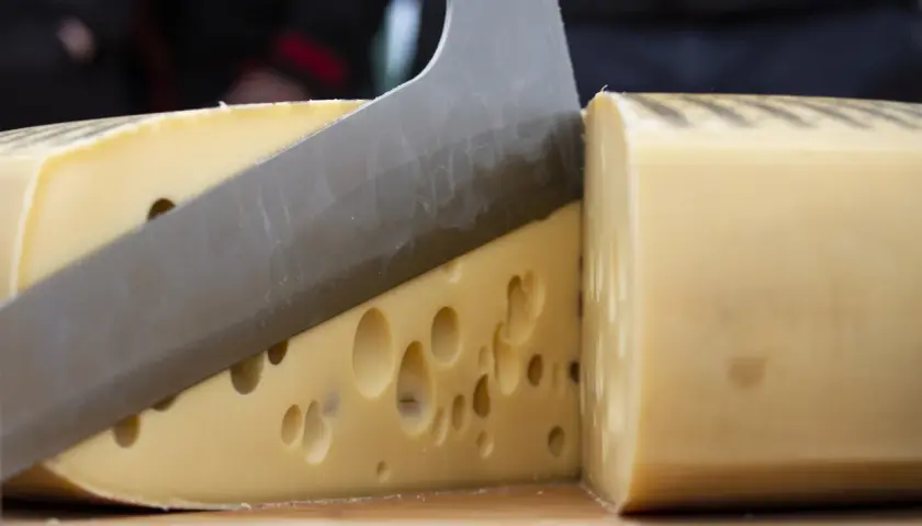 Un coltello affilato taglia un formaggio con i buchi, rivelando la sua consistenza invitante.