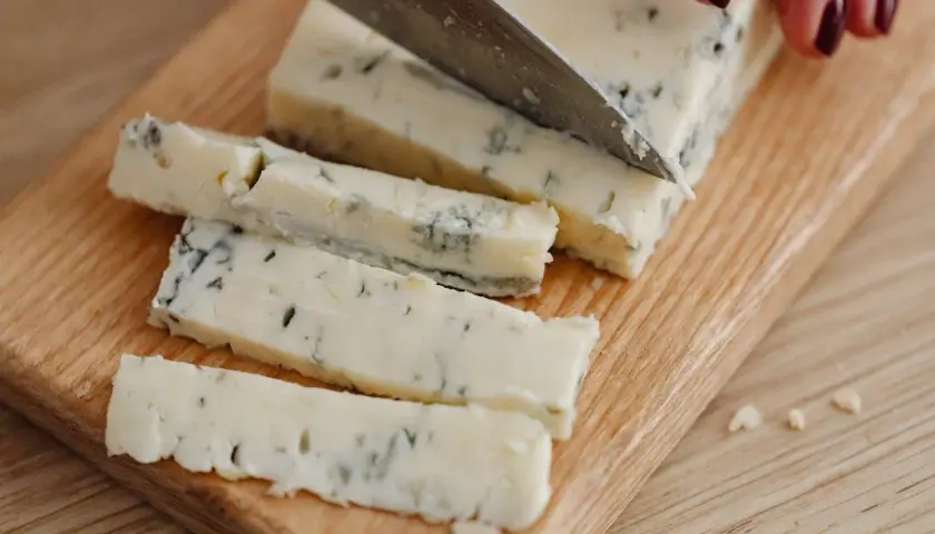 Un pezzo di gorgonzola viene affettato su un tagliere. Un desiderio di gorgonzola in gravidanza, magari per un aperitivo speciale.