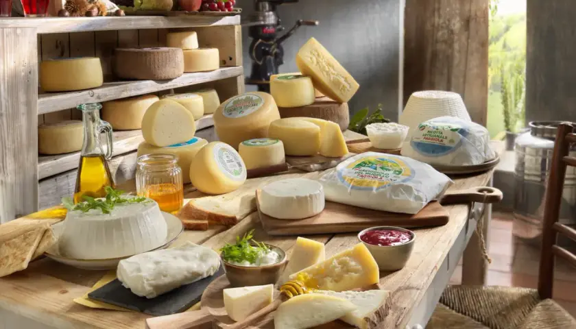 Un ricco elenco formaggi italiani, tra cui freschi e stagionati, disposti su un tavolo di legno con miele, olio e marmellata.