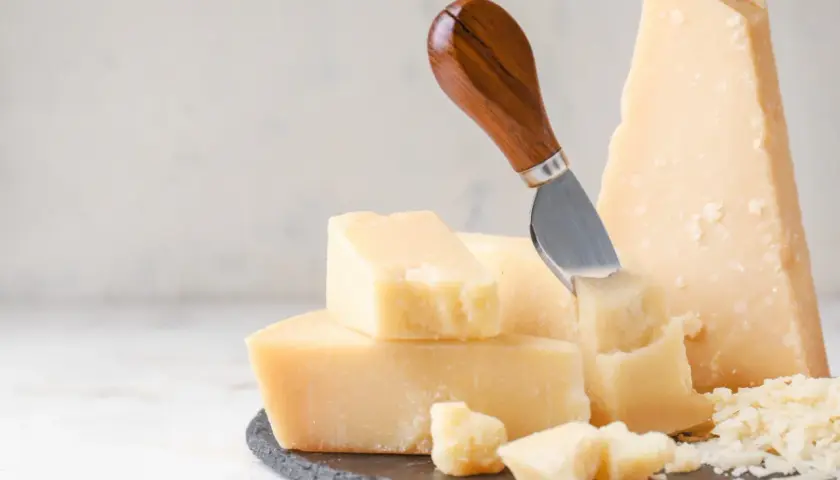 Pezzi di parmigiano reggiano, alcuni grattugiati, con un coltello. Attenzione, il parmigiano contiene lattosio.