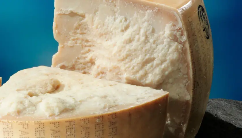 Due pezzi di Parmigiano Reggiano, uno tagliato, mostrano la loro consistenza granulosa. Scopri come conservare il parmigiano in frigo per mantenerlo fresco.