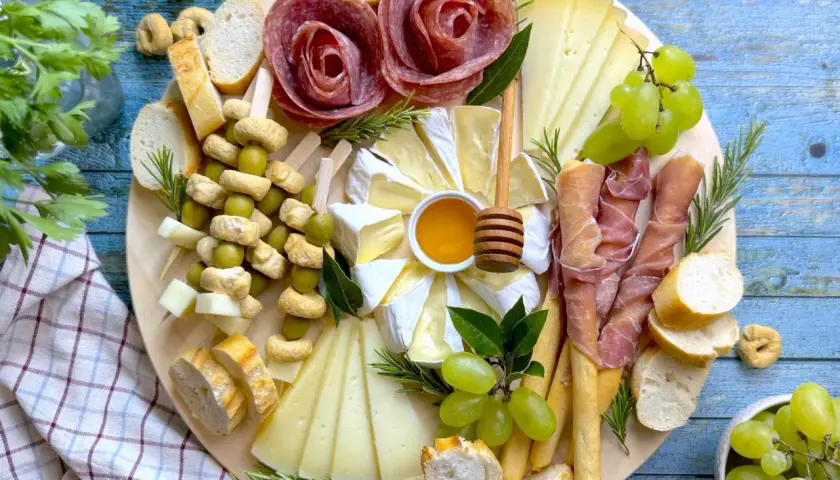 Un vassoio con formaggi, salumi a rosa, uva, olive e pane. Ecco come disporre i salumi nel piatto per un antipasto invitante.