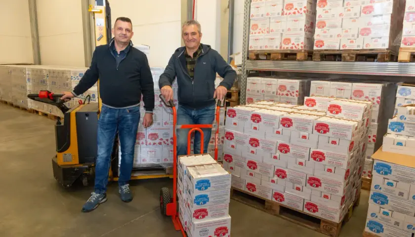 Due uomini in un magazzino con scatoloni di latte a lunga conservazione aperto fuori dal frigo.