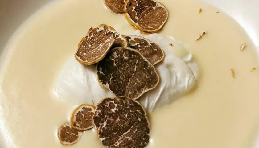 Uovo pochè su una cremosa fonduta, guarnito con scaglie di tartufo nero. Un piatto raffinato e profumato.