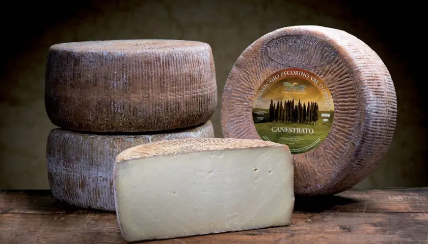 Formaggi di pecorino stagionato, uno intero con etichetta e uno tagliato a cuneo, su un tavolo di legno scuro.