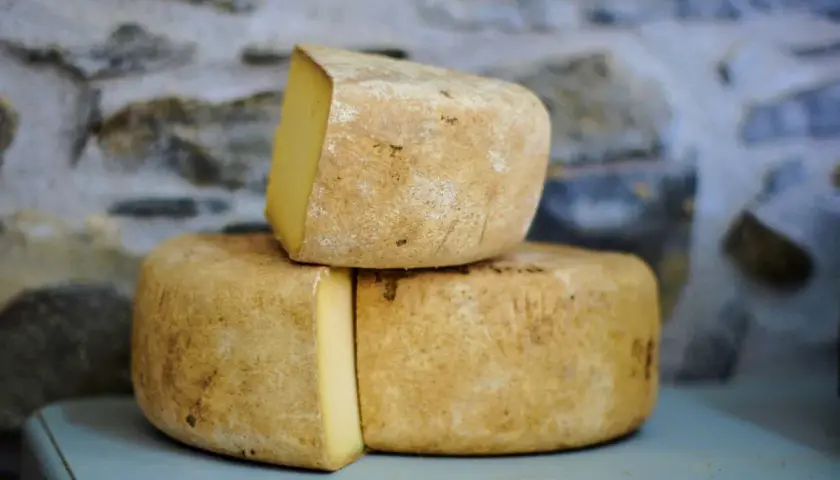 Formaggio di fossa stagionato, con crosta rustica e pasta gialla, impilato su uno sfondo di pietra grezza.