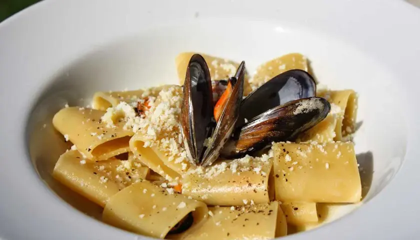 Paccheri con cozze e pecorino, un piatto di pasta saporito e invitante, guarnito con cozze fresche e formaggio grattugiato.