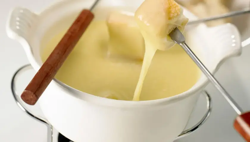 Un pezzo di pane viene intinto in una cremosa fonduta di stracchino, che cola filante.