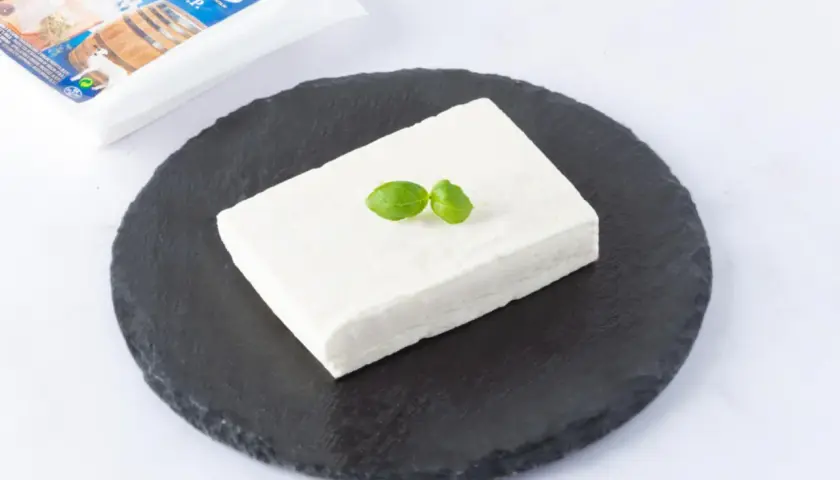 Un blocco di feta DOP su una pietra scura, guarnito con basilico. La confezione è visibile sullo sfondo.