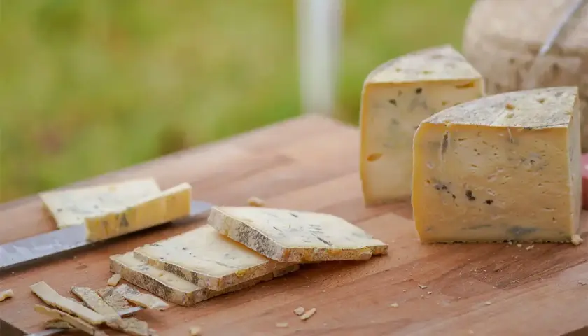 Formaggio stagionato con venature di muffa blu e verde su un tagliere di legno. Alcune fette sono già state tagliate.