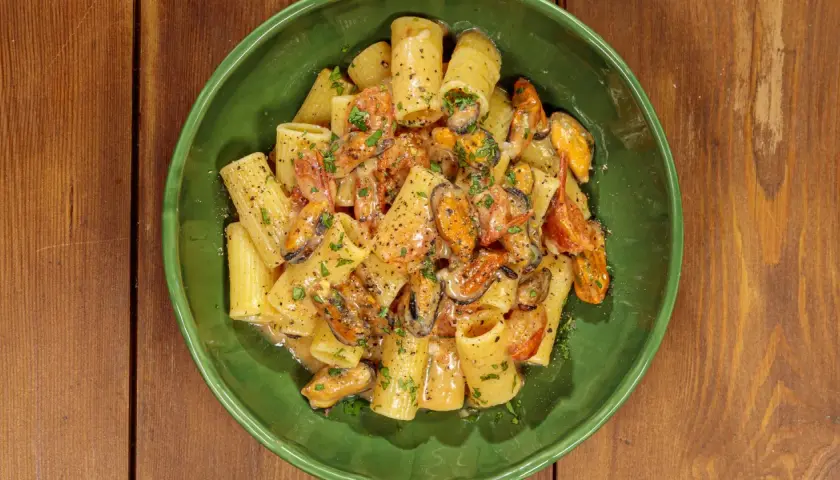 Rigatoni con cozze e pomodorini, conditi con una cremosa salsa al pecorino e prezzemolo fresco.