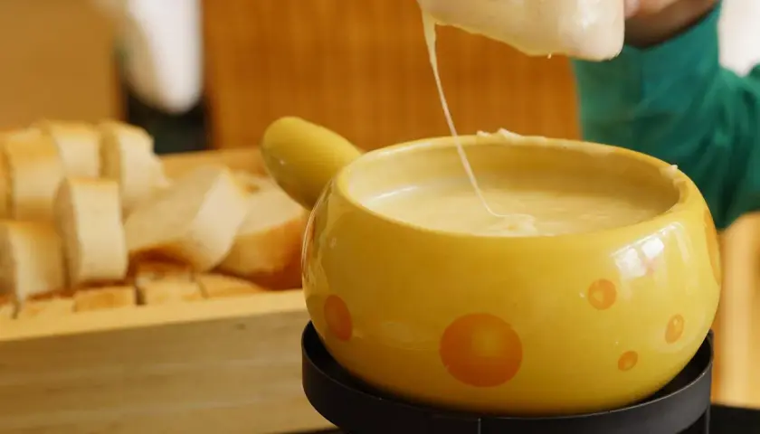 Un pezzo di pane viene intinto in una fonduta di formaggio filante, un modo delizioso per fondere il formaggio.