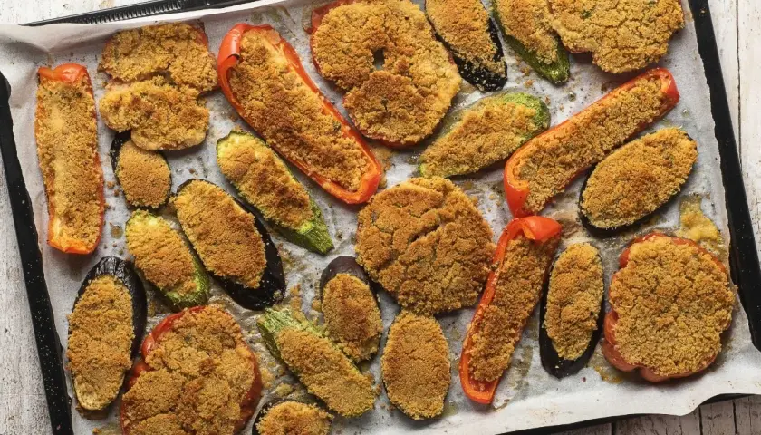 Verdure gratinate al forno con formaggio, un tripudio di sapori e colori su una teglia. Melanzane, zucchine e peperoni ripieni di pangrattato croccante.
