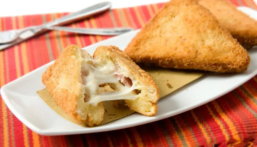 Mozzarella in carrozza dorata e filante, preparata in friggitrice ad aria, servita su un piatto bianco con tovaglietta a righe rosse.