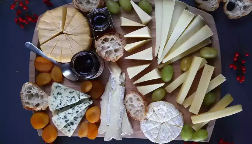 Un tagliere ricco di formaggi francesi, con pane, uva, albicocche secche e marmellata.