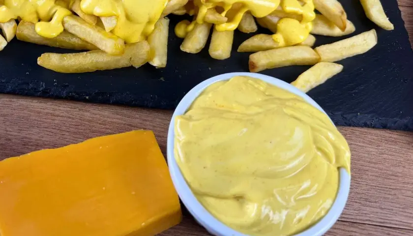 Patatine fritte ricoperte di cremosa salsa cheddar, con un blocco di formaggio e una ciotola di salsa a lato.