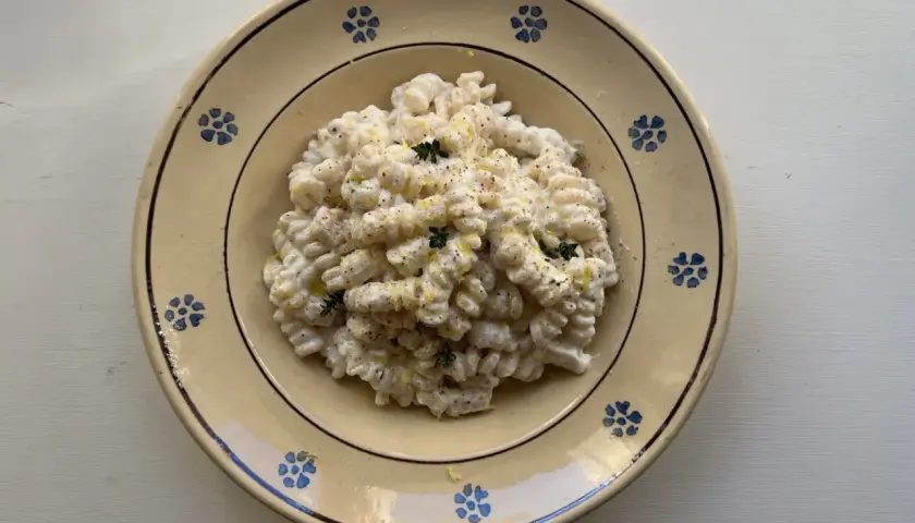 Piatto di pasta ricotta e limone, condita con erbe aromatiche e pepe nero, servita in un piatto di ceramica decorato.