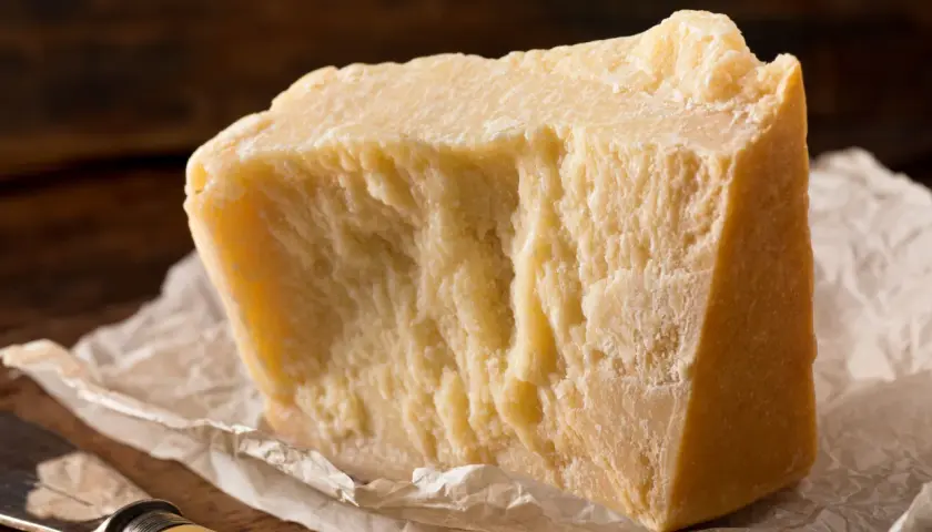 Un pezzo di formaggio stagionato, ideale per chi cerca un formaggio senza lattosio, su carta da forno con un coltello.