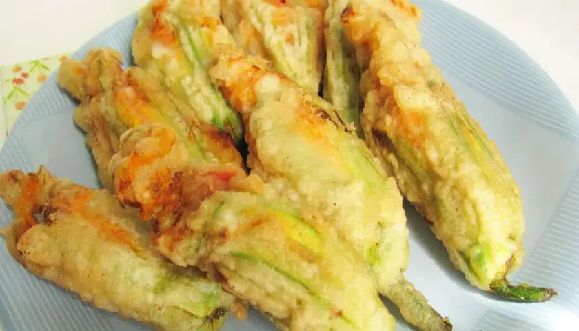Fiori di zucca ripieni di ricotta, dorati e croccanti, serviti su un piatto azzurro.