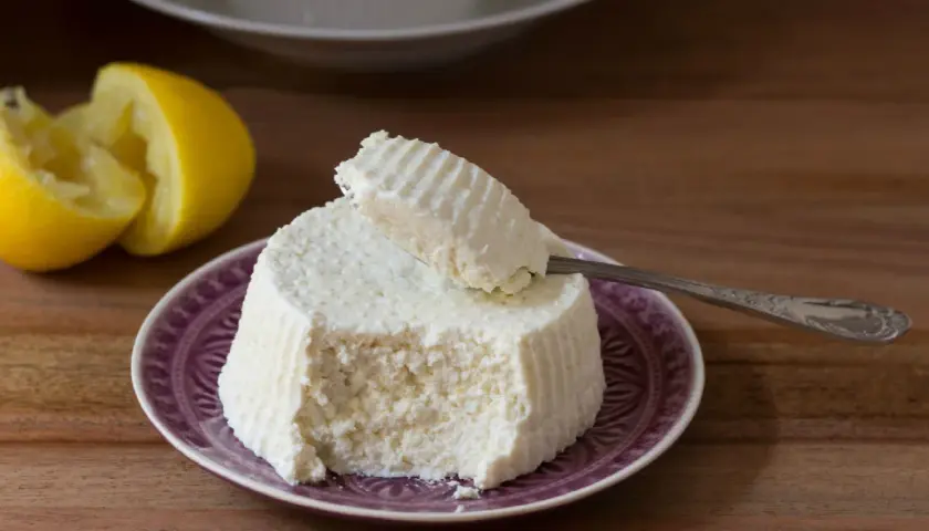 Ricotta fresca su piatto viola, con limone e cucchiaino. Perfetta per ogni ricetta.