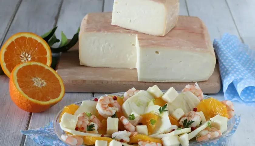 Un blocco di formaggio taleggio stagionato, pronto per essere gustato con un'insalata fresca di arance, finocchi e gamberetti.
