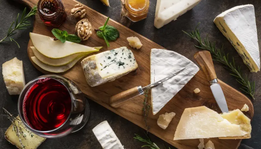 Tagliere con vari formaggi, tra cui un formaggio inglese, pere, noci, miele e vino rosso.