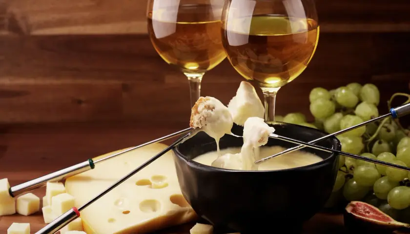 Fonduta di formaggio con pane e uva, accompagnata da vino bianco. Un'ottima fonduta di formaggio con cosa si accompagna? Con questi ingredienti, è perfetta!