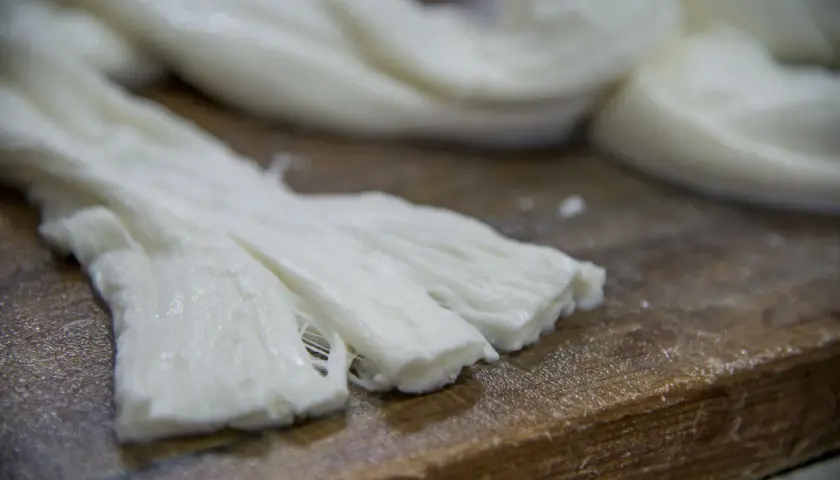Formaggio a pasta filata, lavorato a mano, con fili bianchi e morbidi su un tagliere di legno.