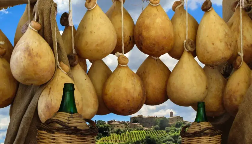 Formaggio cacio appeso, con sfondo di un borgo toscano e vigneti.