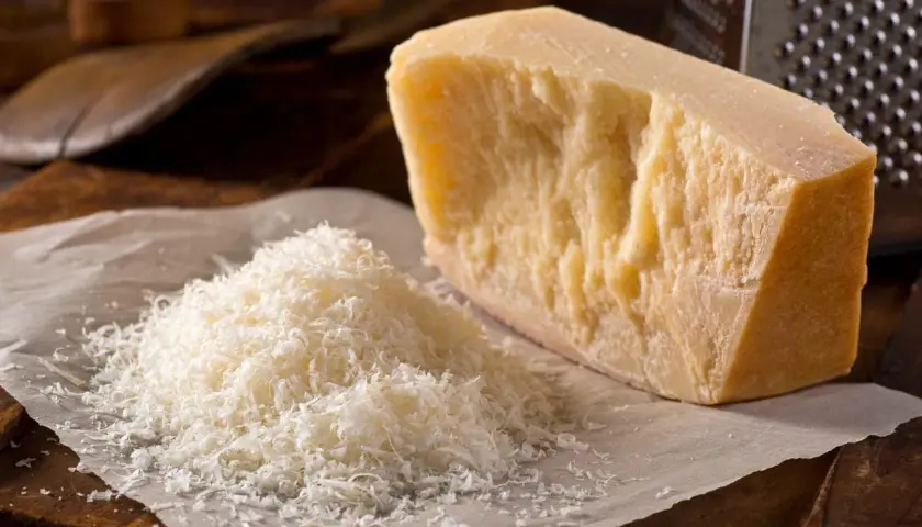 Un pezzo di Parmigiano Reggiano accanto a una montagnetta di formaggio grattugiato. Si può congelare il parmigiano grattugiato per averlo sempre pronto.